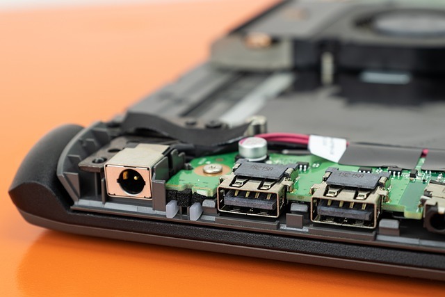 Wnętrze laptopa z widocznymi portami USB i złączem zasilania, ukazujące płytę główną i elementy elektroniczne w trakcie naprawy lub diagnostyki.