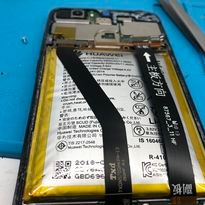 Otwarty smartfon Huawei z widoczną baterią i elementami wewnętrznymi, przygotowywany do naprawy. Na baterii widoczne czarne taśmy i napisy w języku chińskim. W tle leżą narzędzia serwisowe.