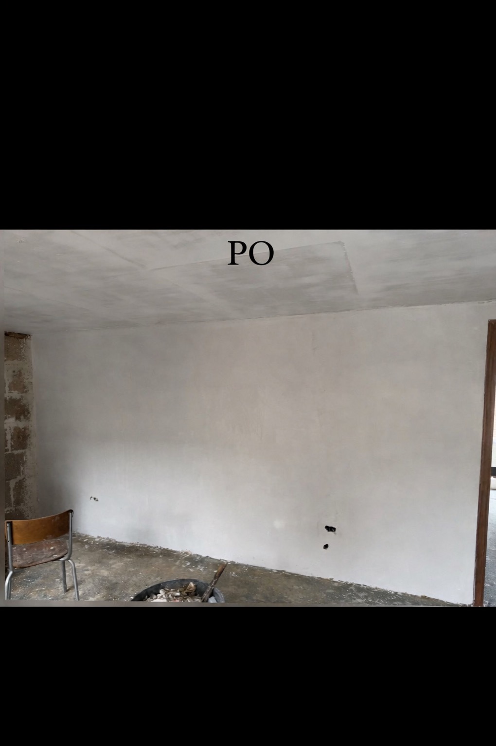 Wnętrze po remoncie: gładkie, białe ściany i sufit. Widoczny fragment ściany z cegły, krzesło i wiadro z narzędziami. Ujęcie z napisem 'PO' na suficie.