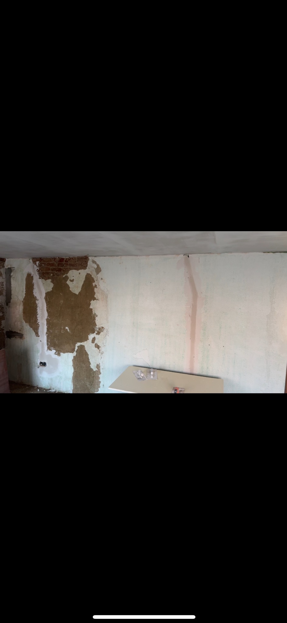 Ściana w trakcie remontu: częściowo otynkowana, z widoczną cegłą i instalacją elektryczną. Na podłodze leżą płyty gipsowe i akcesoria.