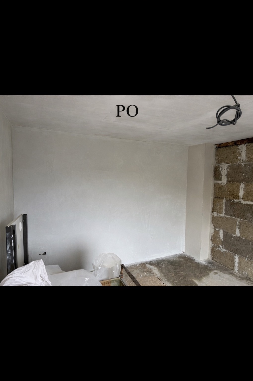 Wnętrze po remoncie: gładkie, białe ściany i sufit. Fragment ściany z surowej cegły. Widoczne zabezpieczenia podłogi i materiały budowlane. Ujęcie z napisem 'PO'.