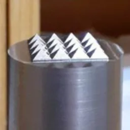 Metalowy stempel z rzędem trójkątnych ostrzy, widoczne ślady obróbki na powierzchni cylindrycznej podstawy.