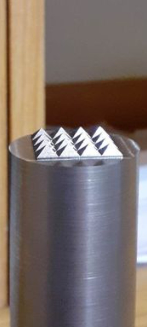 Metalowy stempel z rzędem trójkątnych ostrzy, widoczne ślady obróbki na powierzchni cylindrycznej podstawy.