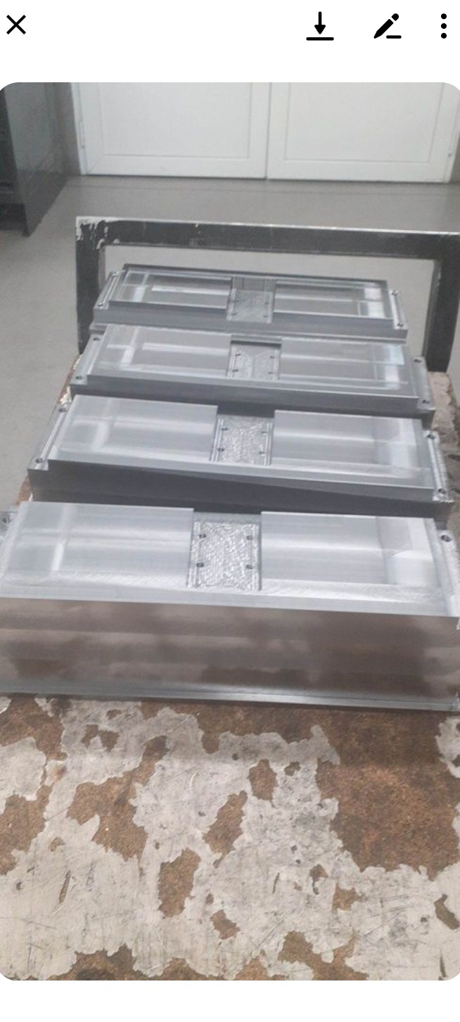 Szare, metalowe formy odlewnicze ułożone jedna na drugiej na brudnym stole, widoczne ślady obróbki i mocowania.