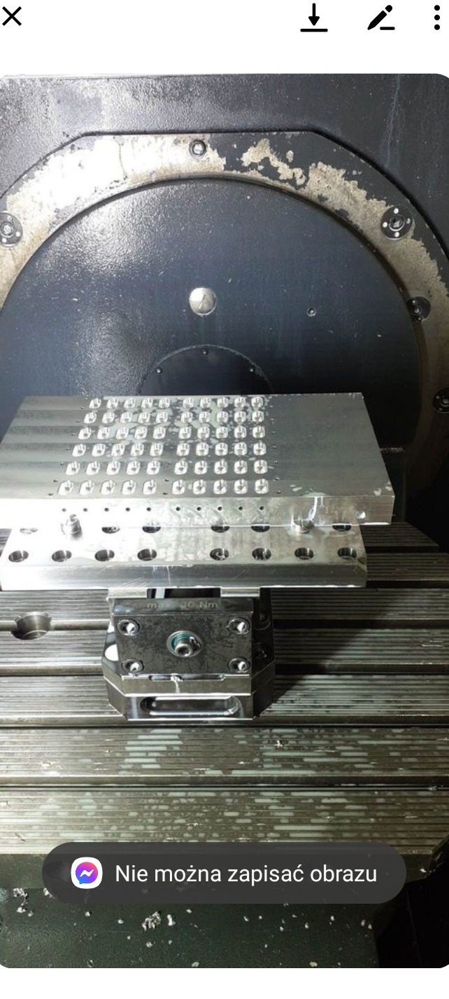 Metalowy element z szeregiem wyfrezowanych otworów, zamocowany na stole maszyny CNC, widok z bliska.