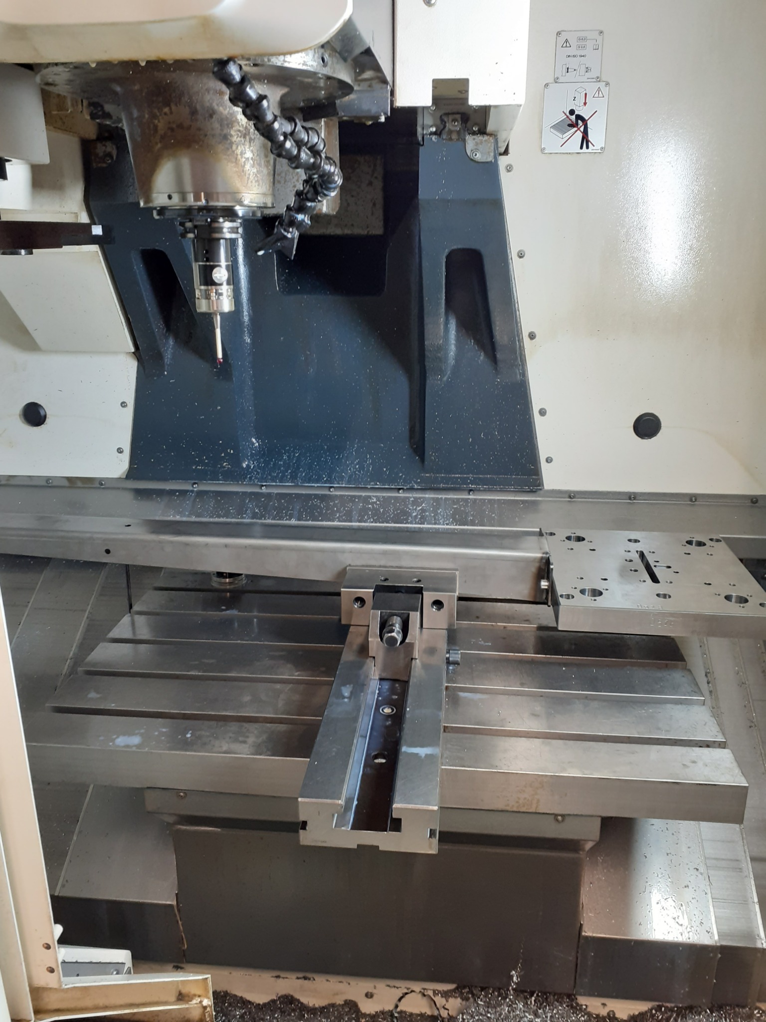 Frezarka CNC z zamocowanym elementem, widoczne ślady obróbki i chłodziwa na stole roboczym.