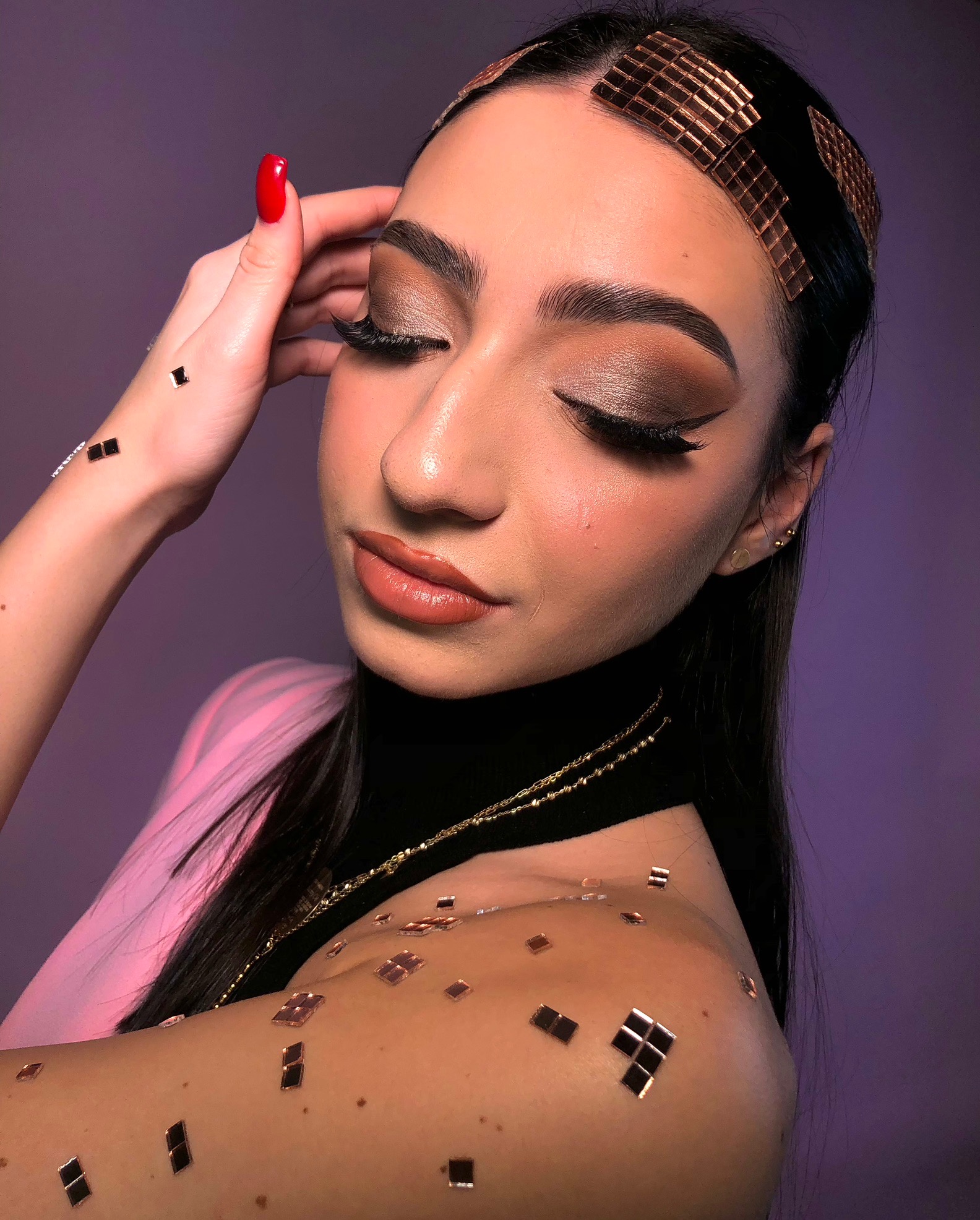 Portret kobiety z zamkniętymi oczami, w pełnym makijażu oczu w odcieniach brązu, z błyszczącymi detalami na twarzy i włosach, oraz czerwonym manicure.