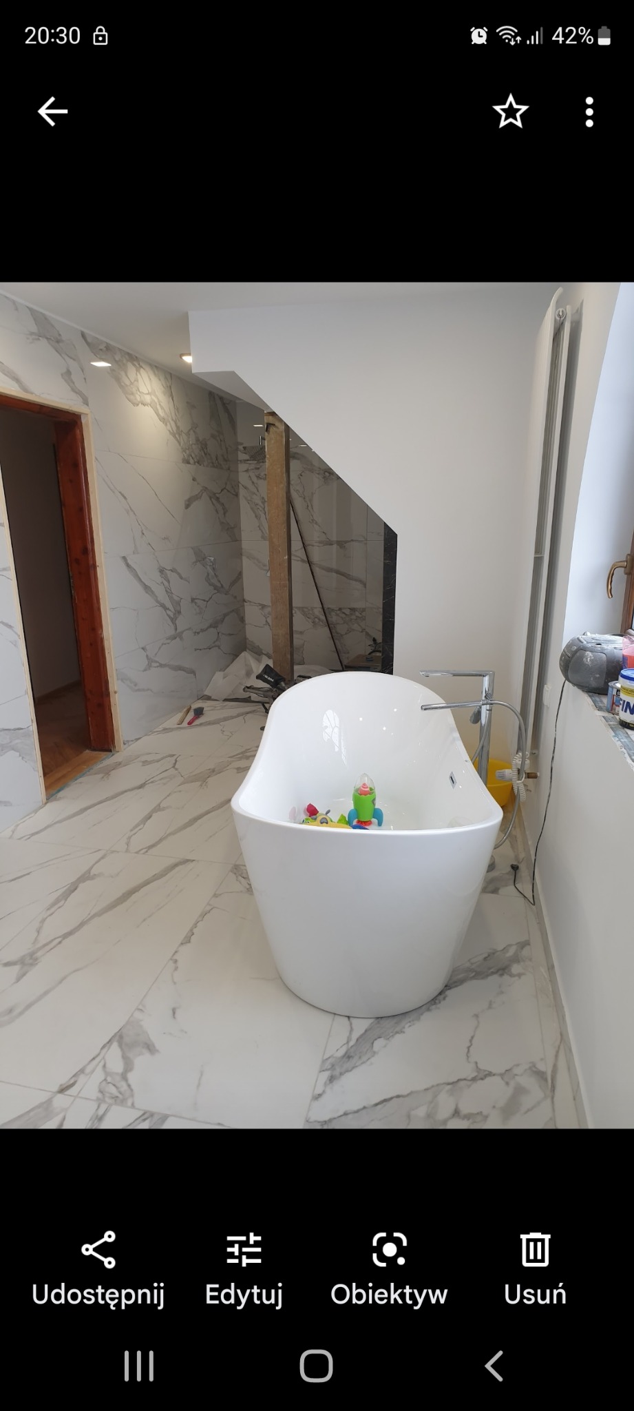 Nowogard: Nowoczesna, wolnostojąca wanna wypełniona zabawkami w łazience z marmurowymi płytkami, w trakcie prac wykończeniowych.