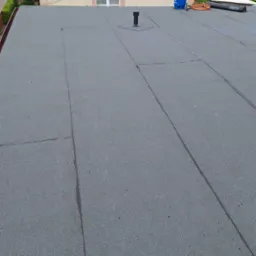 Szary, płaski dach pokryty papą termozgrzewalną z widoczną butlą gazową i zwiniętą rolką papy w tle.