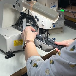 HATEX SPÓŁKA Z OGRANICZONĄ ODPOWIEDZIALNOŚCIĄ - Praca przy maszynie szwalniczej JUKI: szycie czarnego zamka błyskawicznego. Widoczne dłonie, zegarek na ręce, ubranie w ananasy. Oświetlenie LED maszyny.