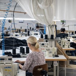 HATEX SPÓŁKA Z OGRANICZONĄ ODPOWIEDZIALNOŚCIĄ - Szwalnia odzieży ciężkiej: pracownice przy maszynach JUKI i PFAFF, czarne nici i materiały. Jasne, przestronne wnętrze z oświetleniem przemysłowym.