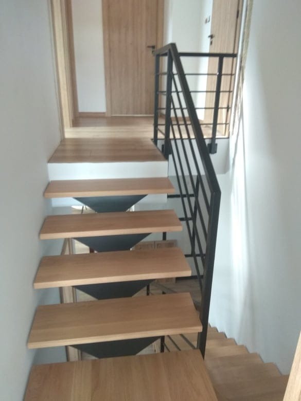 Schody drewniane z metalową balustradą w nowoczesnym wnętrzu, widok z dołu na górę, jasne drewno i czarne metalowe elementy.