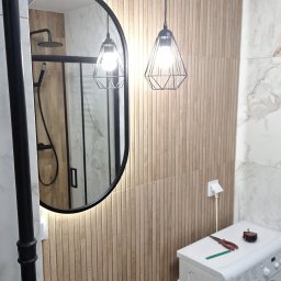 Usługi Remontowo Budowlane Paweł Gacek - Nowoczesna łazienka z umywalką w lustrze, oświetleniem wiszącym i pralką z narzędziami na górze.