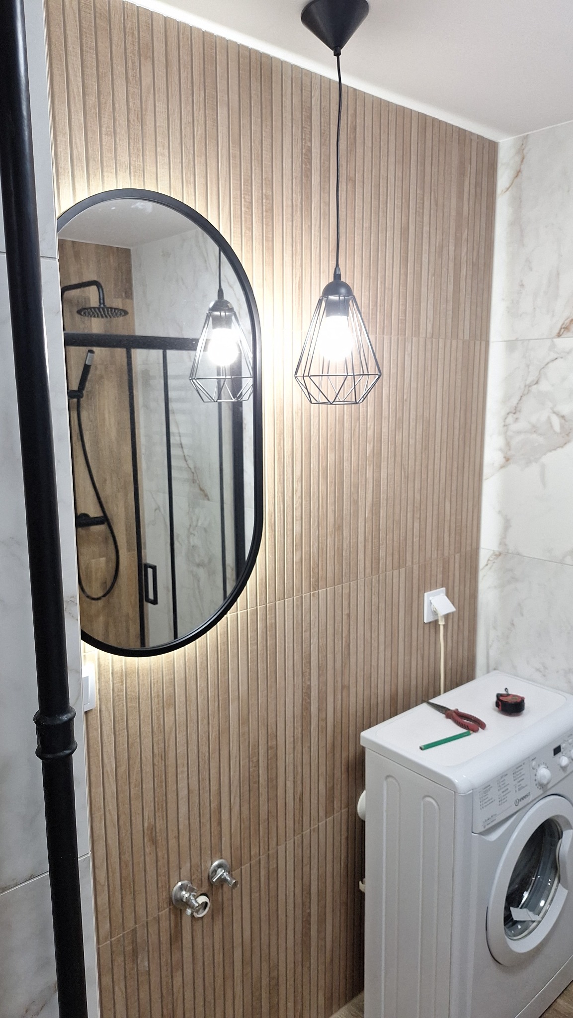 Nowoczesna łazienka z umywalką w lustrze, oświetleniem wiszącym i pralką z narzędziami na górze.