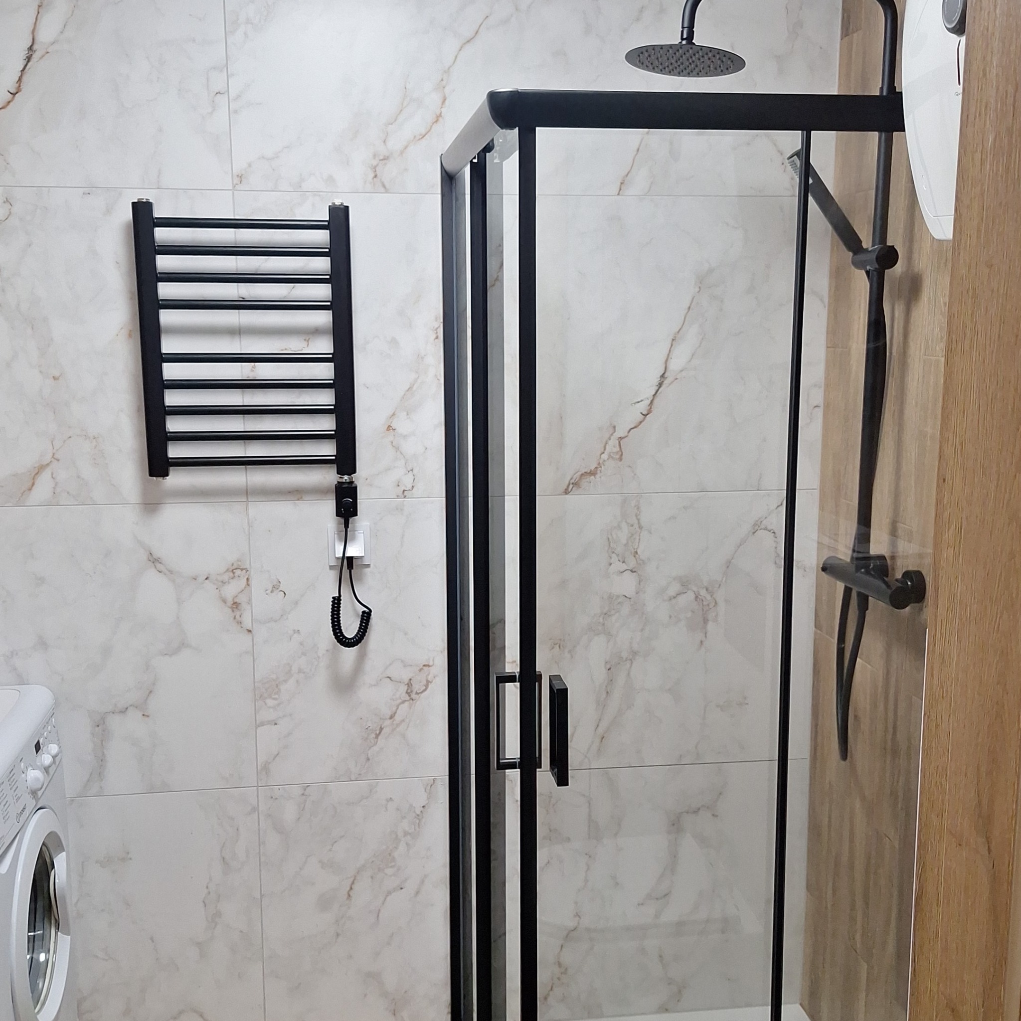 Nowoczesna łazienka z kabiną prysznicową z czarnymi ramami, grzejnikiem drabinkowym i marmurowymi płytkami ściennymi.