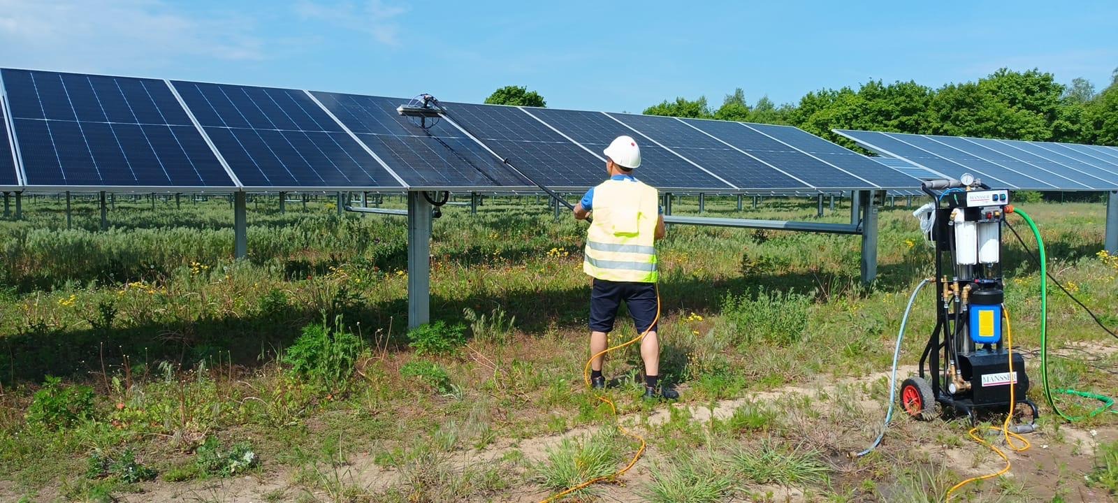Czyszczenie paneli fotowoltaicznych w Szamotułach. Pracownik w kasku i kamizelce odblaskowej myje panele za pomocą specjalistycznego sprzętu.