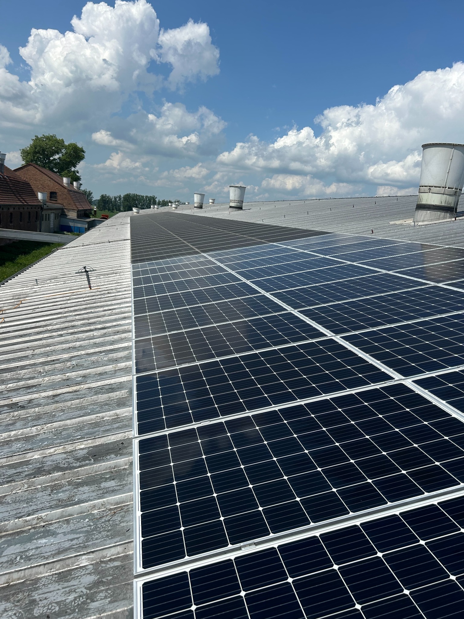 Częściowo umyte panele słoneczne na metalowym dachu, widoczne różnice w czystości, błękitne niebo z chmurami w tle.