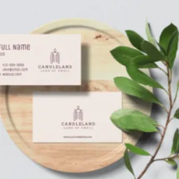 Dwie wizytówki firmy Candieland na drewnianej tacy z zieloną gałązką, prezentujące logo i dane kontaktowe.
