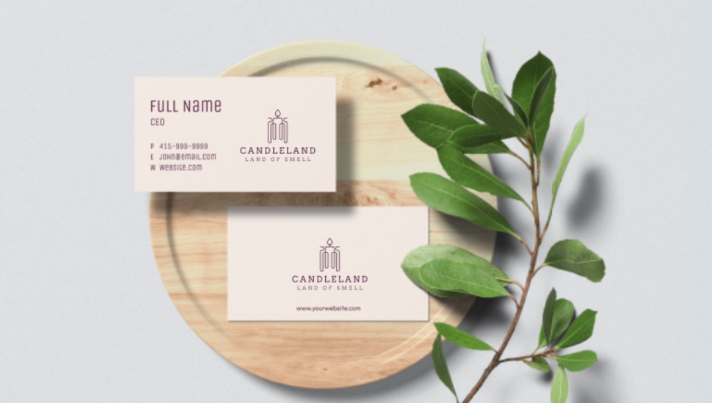 Dwie wizytówki firmy Candieland na drewnianej tacy z zieloną gałązką, prezentujące logo i dane kontaktowe.