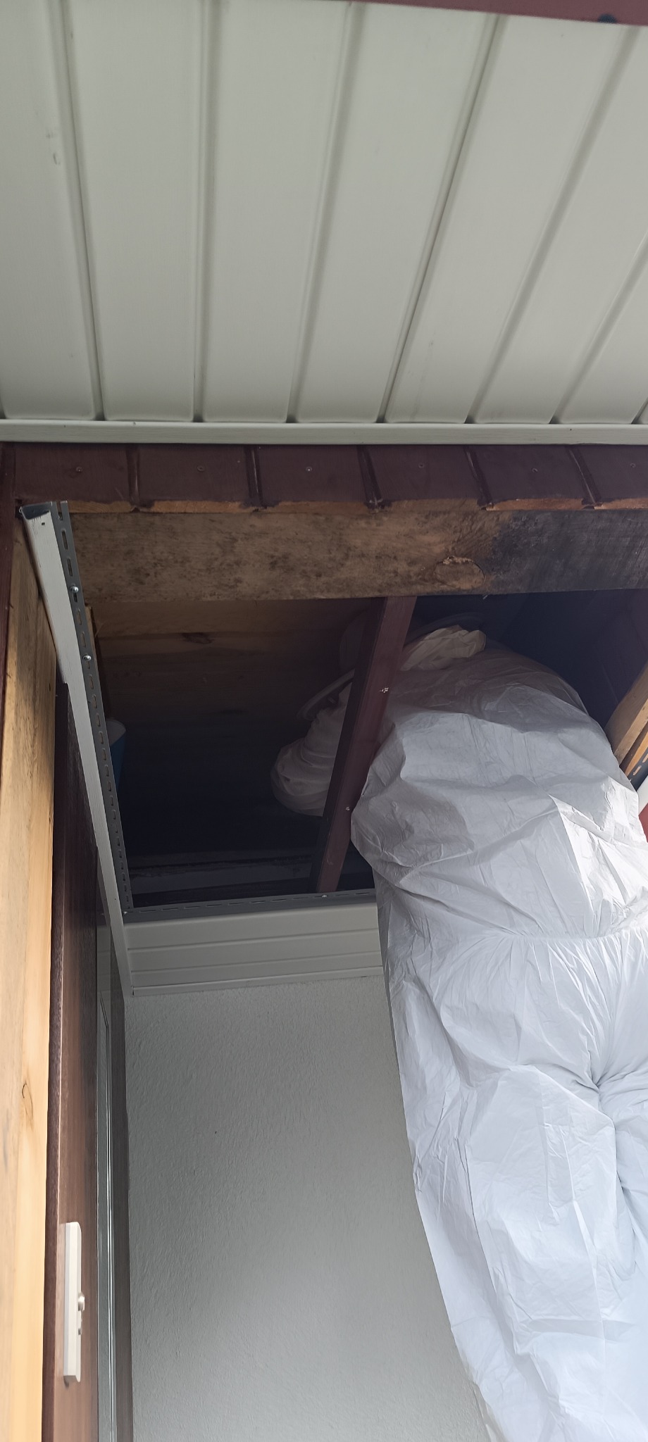 Pracownik w kombinezonie ochronnym wchodzi do przestrzeni pod stropem podczas prac w budynku.