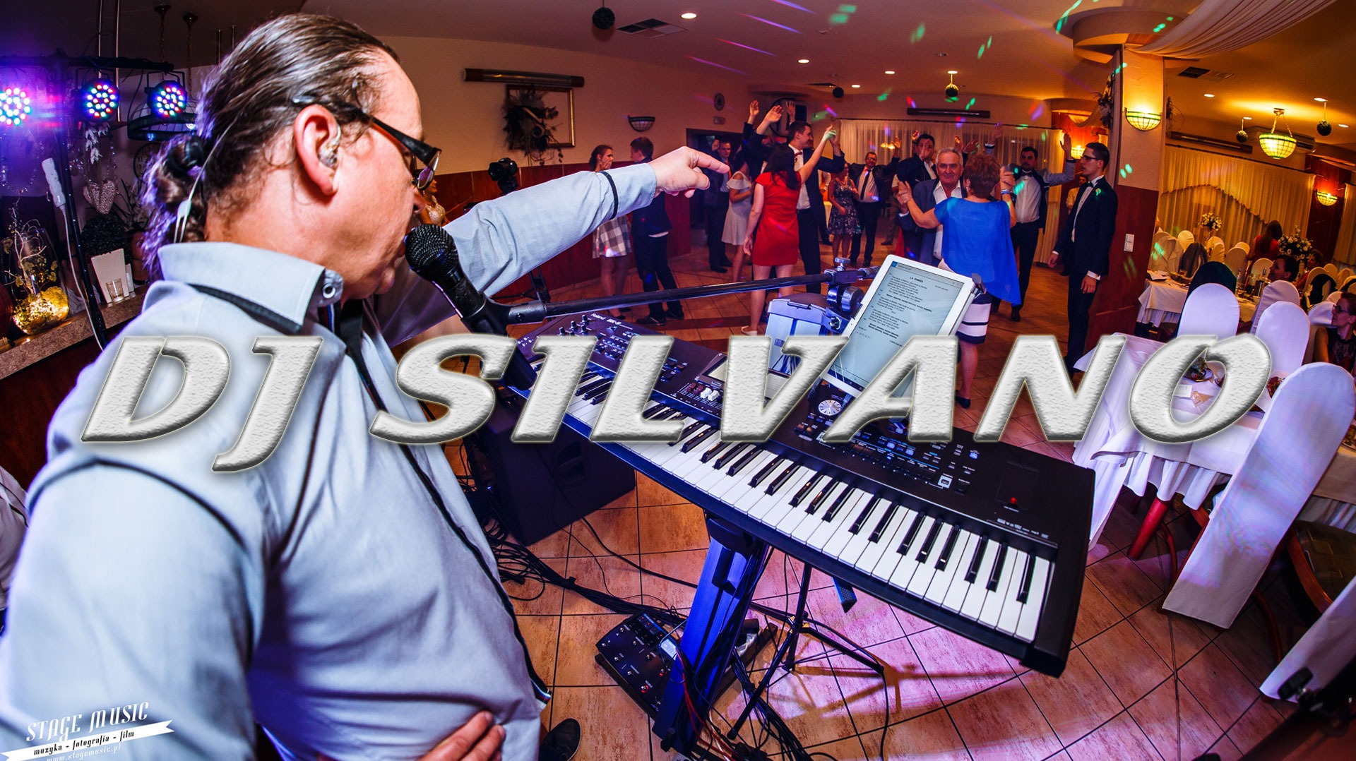 DJ z mikrofonem i klawiszami podczas występu na sali balowej, w tle tańczący goście i kolorowe światła.