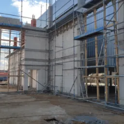 Wznoszenie ścian budynku z betonu komórkowego na placu budowy, widoczne rusztowania i niezabezpieczone otwory okienne.