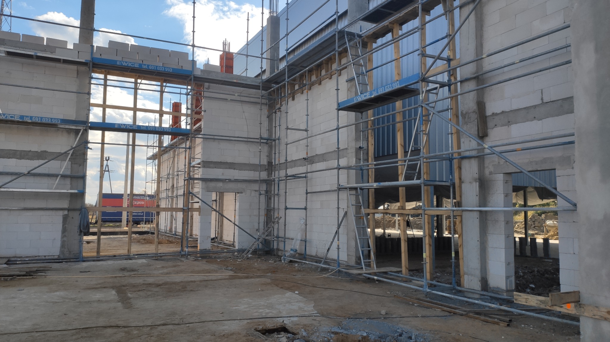 Wznoszenie ścian budynku z betonu komórkowego na placu budowy, widoczne rusztowania i niezabezpieczone otwory okienne.