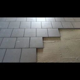 Układanie szarych płytek podłogowych na kleju z widocznymi śladami pacy, w trakcie remontu.