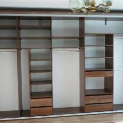 Wnętrze brązowej szafy przesuwnej z półkami i szufladami, widok z dołu na sufit z lampą. Część półek jest pusta, a szuflady zamknięte.