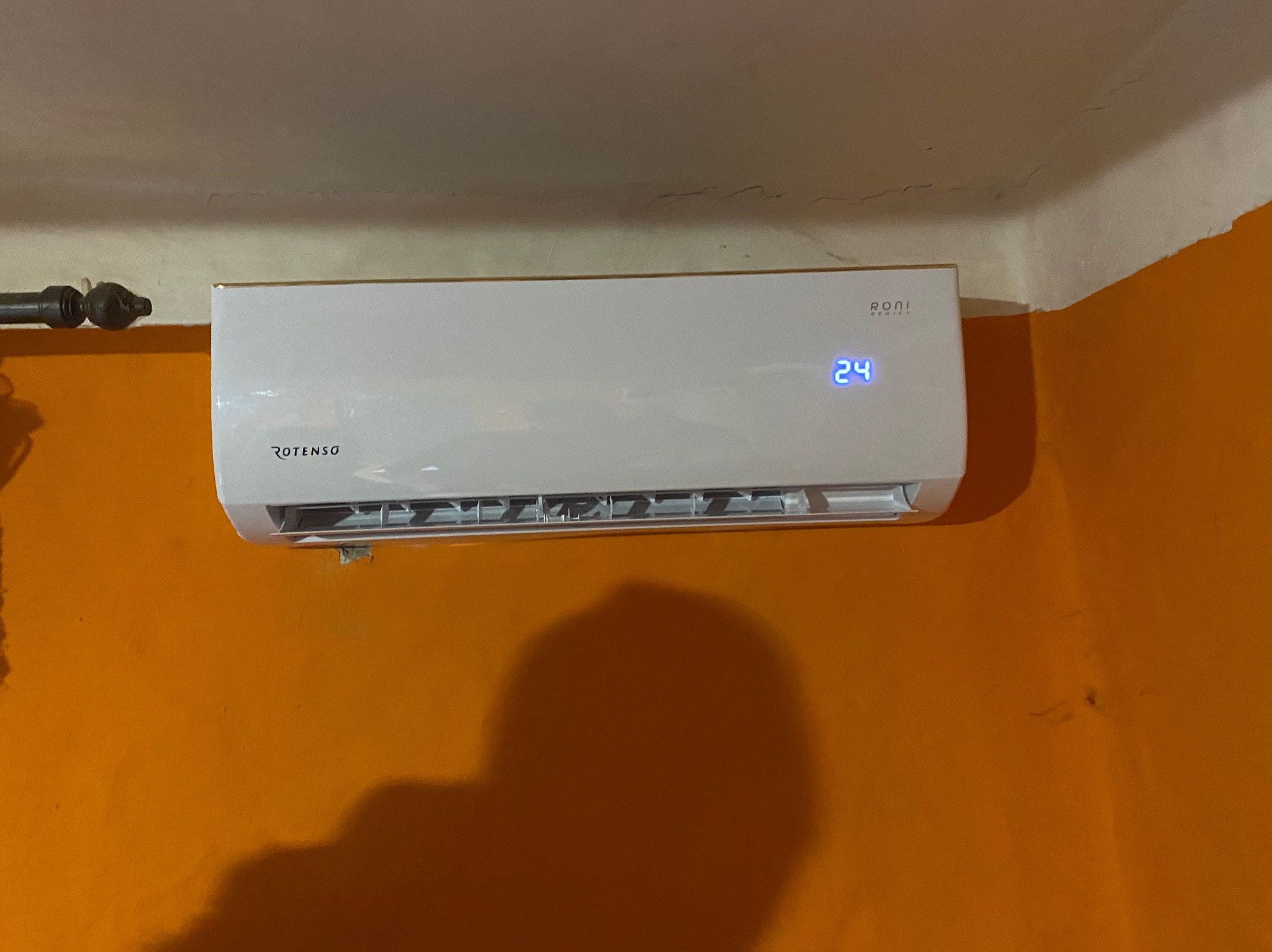 Biały klimatyzator Rotenso zamontowany na pomarańczowej ścianie, widoczny wyświetlacz z temperaturą 24 stopnie.