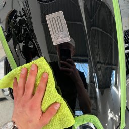 Yauheni Mardasevich - Czyszczenie lakieru motocykla BMW, zabezpieczonego taśmą, miękką, zieloną ściereczką z mikrofibry, widoczny zegarek na ręce osoby wykonującej.