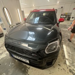 Yauheni Mardasevich - Czarny Mini Cooper z czerwonym dachem po zabiegach detailingu, widoczne odbicia w lakierze, na podłodze ślady po pracy.