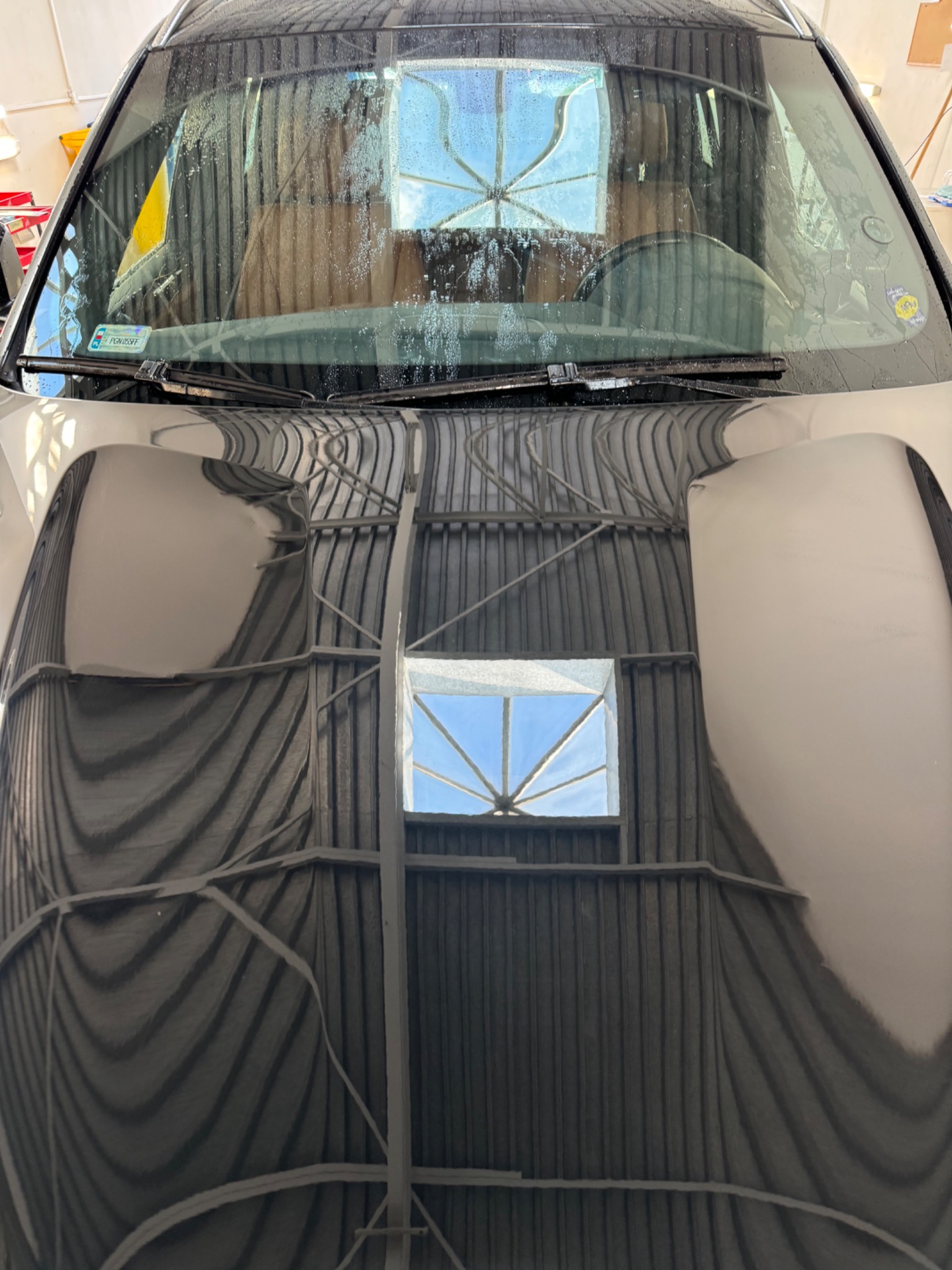 Mokra maska samochodu odbijająca konstrukcję metalowego dachu i okno dachowe z błękitnym niebem.