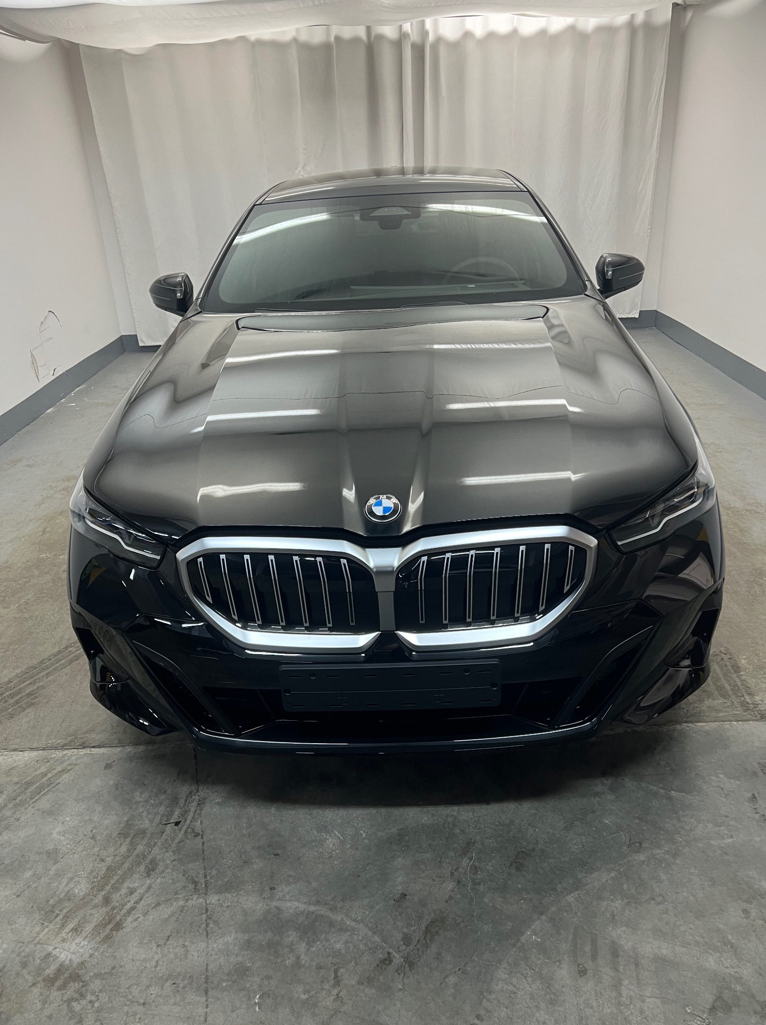 Błyszczący czarny samochód BMW, widok z przodu, po umyciu w myjni, z widocznymi śladami wody na karoserii.