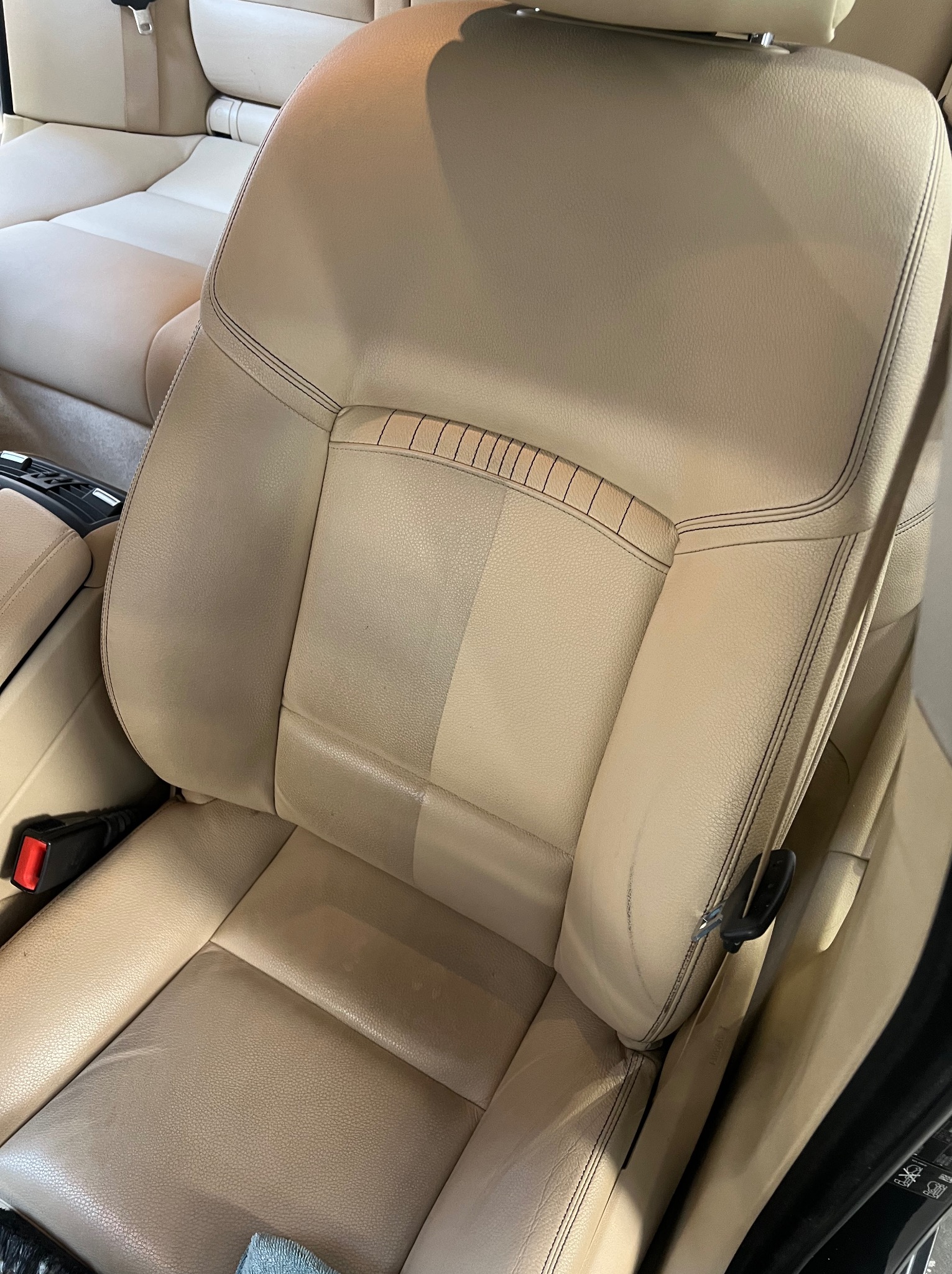 Beżowe skórzane siedzenie samochodowe, widoczna różnica w czystości między wyczyszczoną a zabrudzoną częścią, ukazująca efekt usługi.