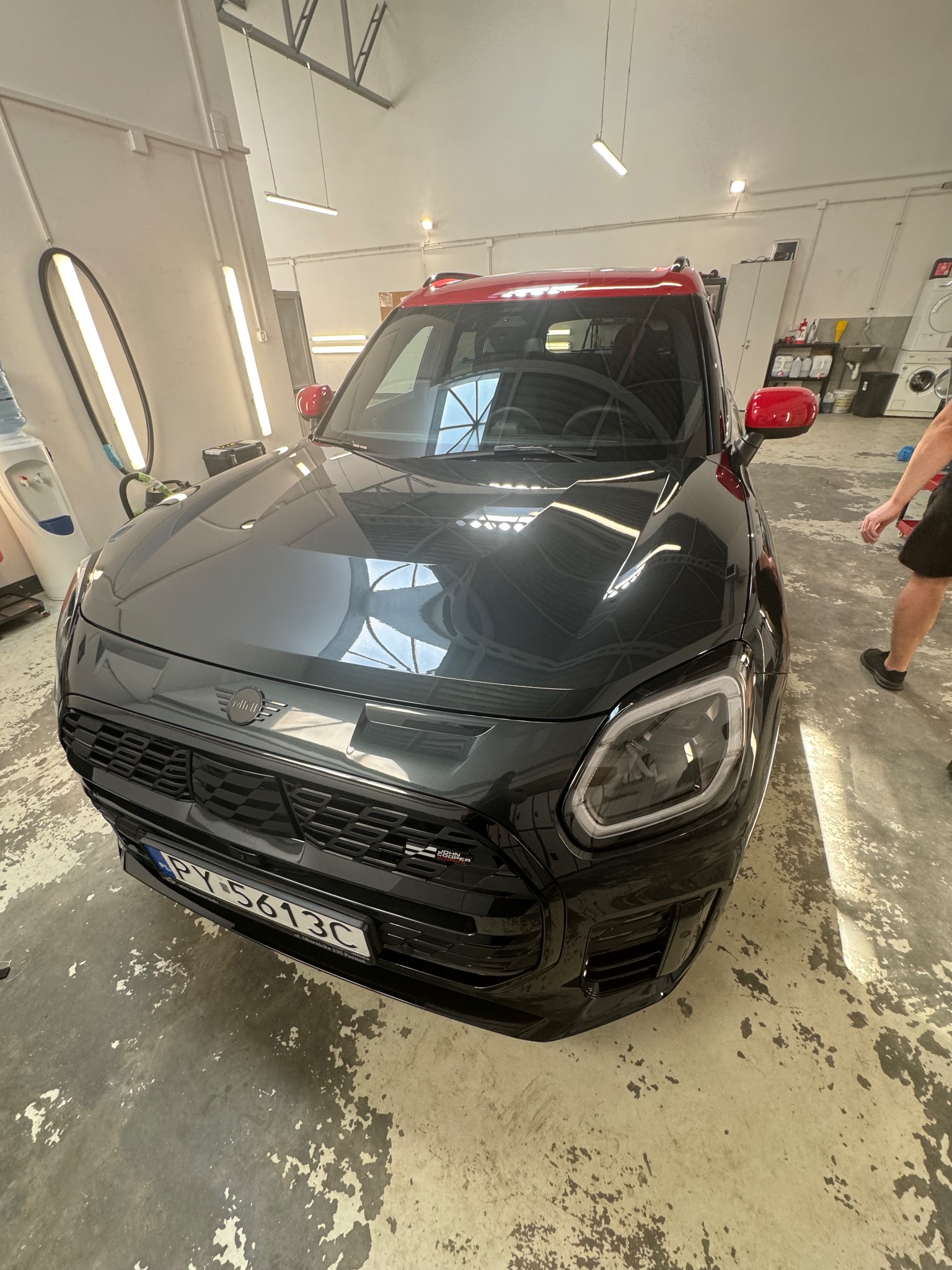 Czarny Mini Cooper z czerwonym dachem po zabiegach detailingu, widoczne odbicia w lakierze, na podłodze ślady po pracy.