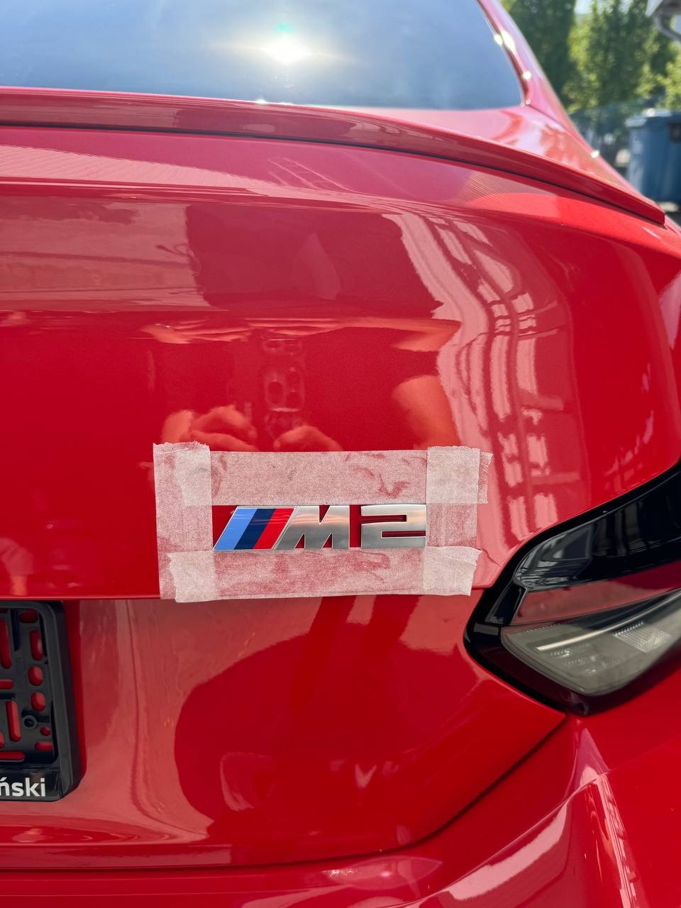 Czerwony samochód marki BMW z naklejonym taśmą nowym znaczkiem M2 na klapie bagażnika.
