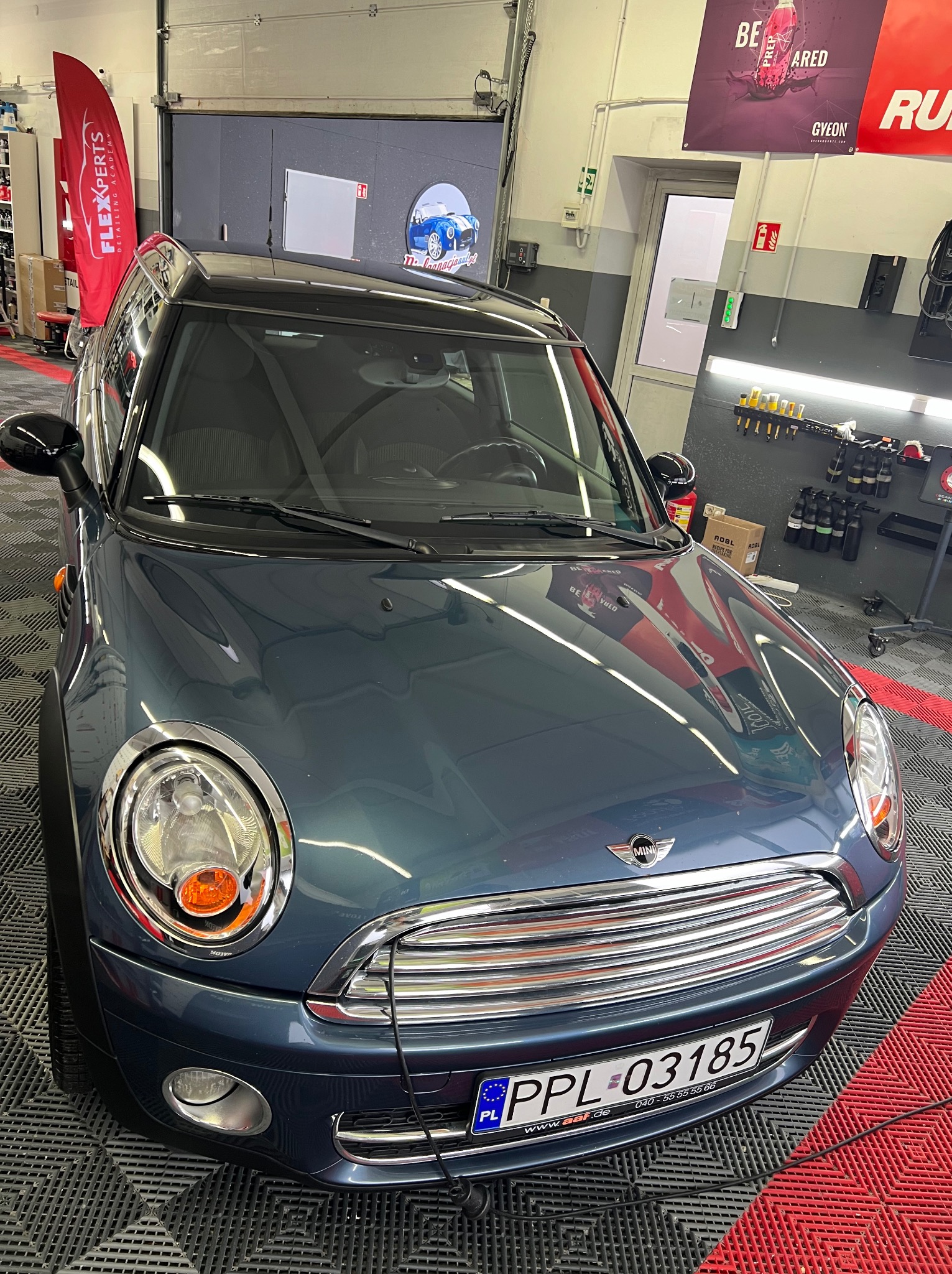 Błękitny Mini Cooper po zabiegach pielęgnacyjnych, widoczny w detalingowym studiu z refleksami światła na karoserii i tablicą rejestracyjną PPL 03185.