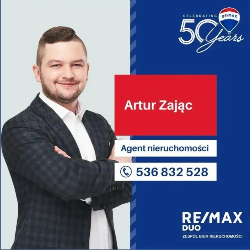 Portret uśmiechniętego agenta nieruchomości, Artur Zając, na tle z logo RE/MAX i numerem telefonu.