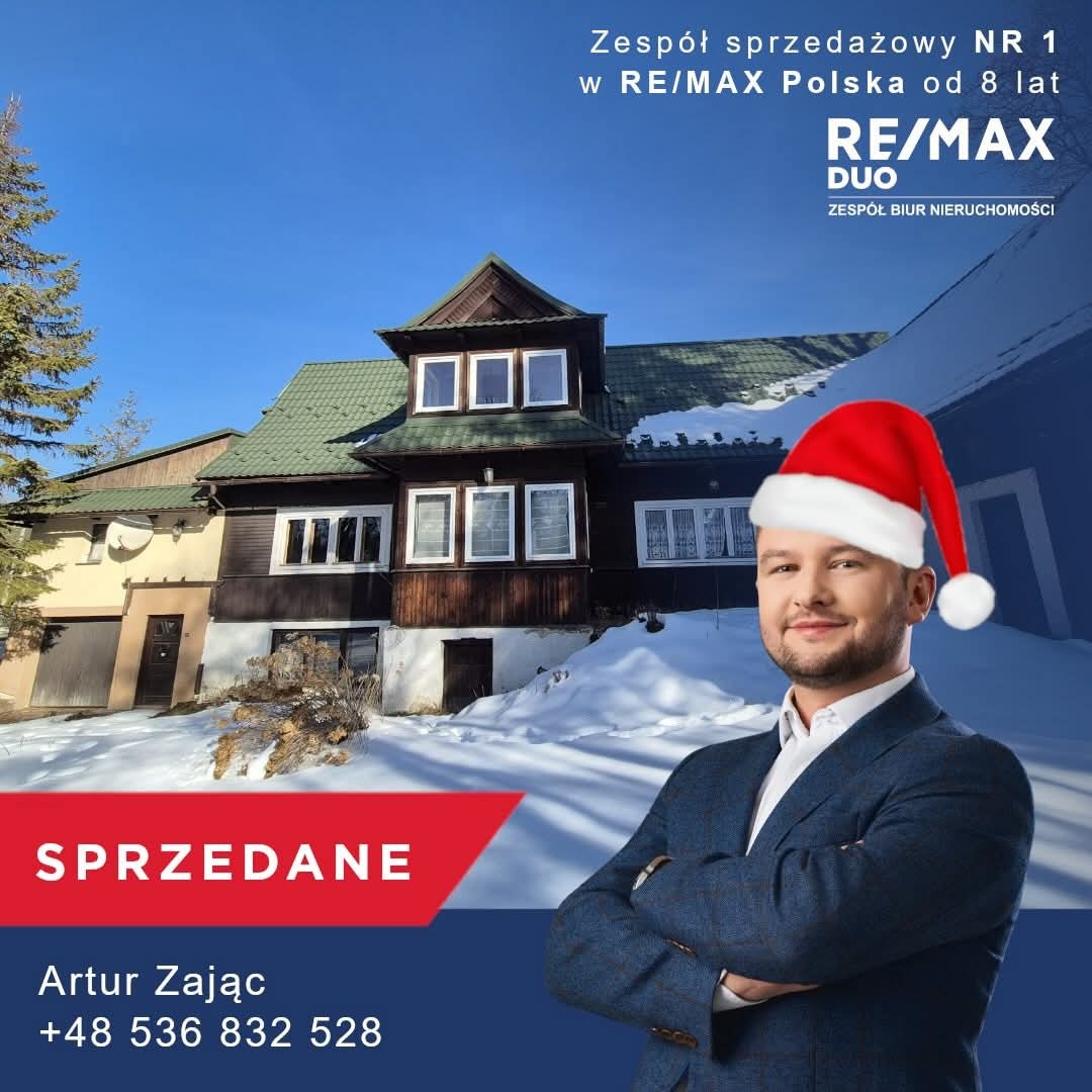 Agent nieruchomości w czapce Mikołaja na tle sprzedanego, zimowego domu w stylu góralskim. Logo RE/MAX DUO i napis SPRZEDANE.