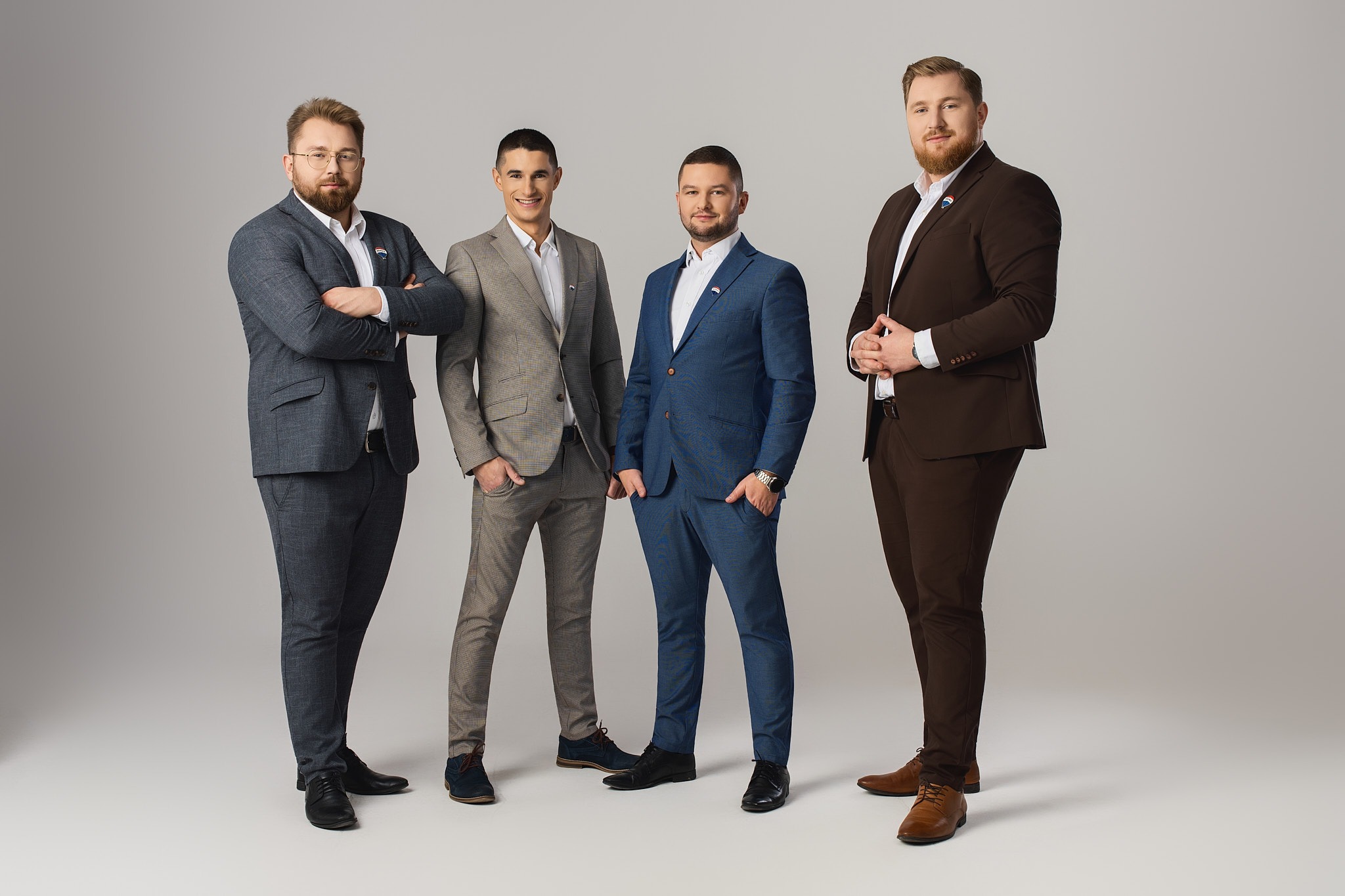 Czterech eleganckich mężczyzn w garniturach, z przypinkami RE/MAX, pozuje na jasnym tle. Zespół agentów nieruchomości prezentuje profesjonalizm i zgranie.