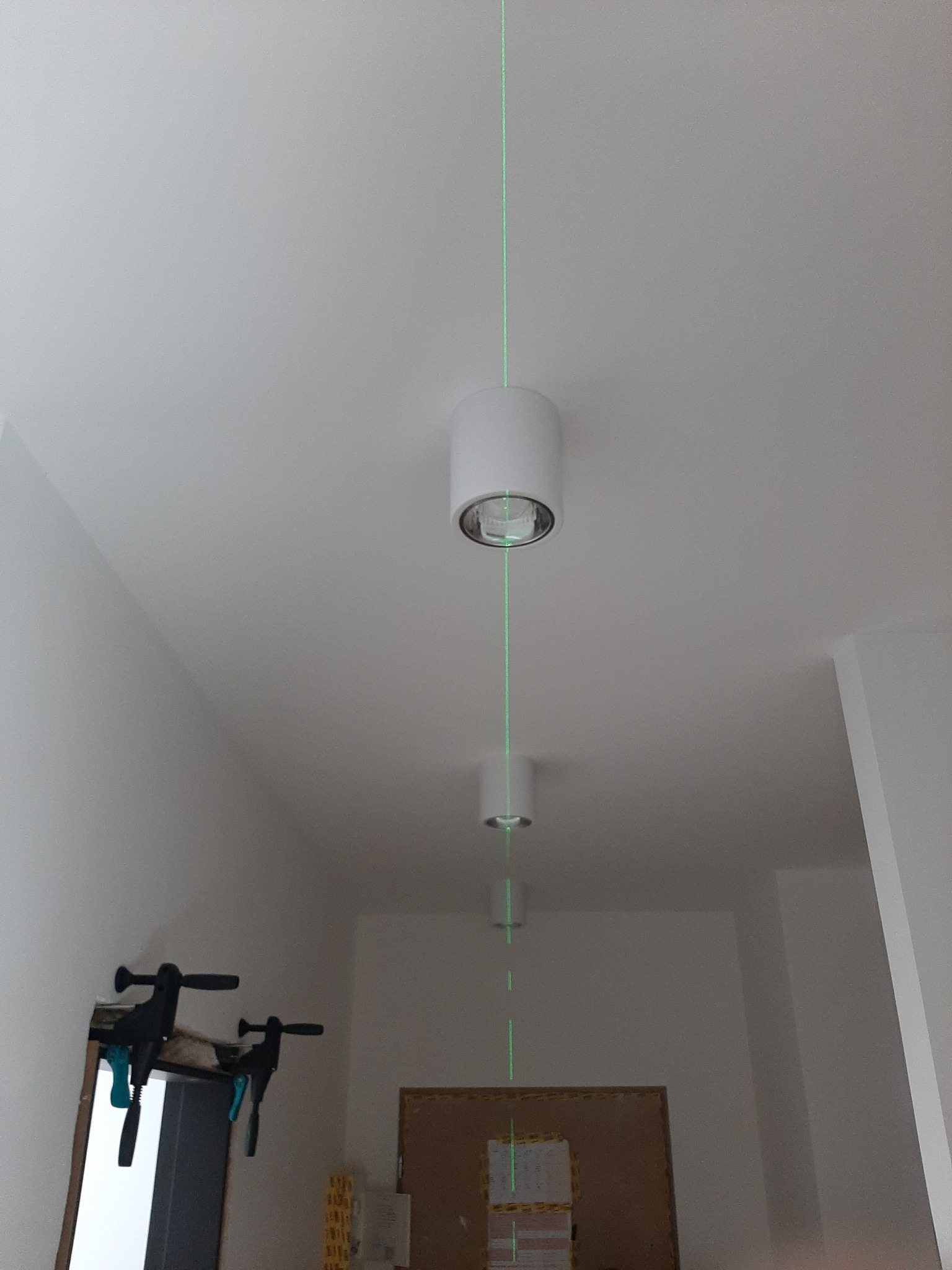 Montaż oświetlenia sufitowego w korytarzu, widoczna linia lasera wyznaczająca poziom, białe lampy tuby zamontowane w suficie.