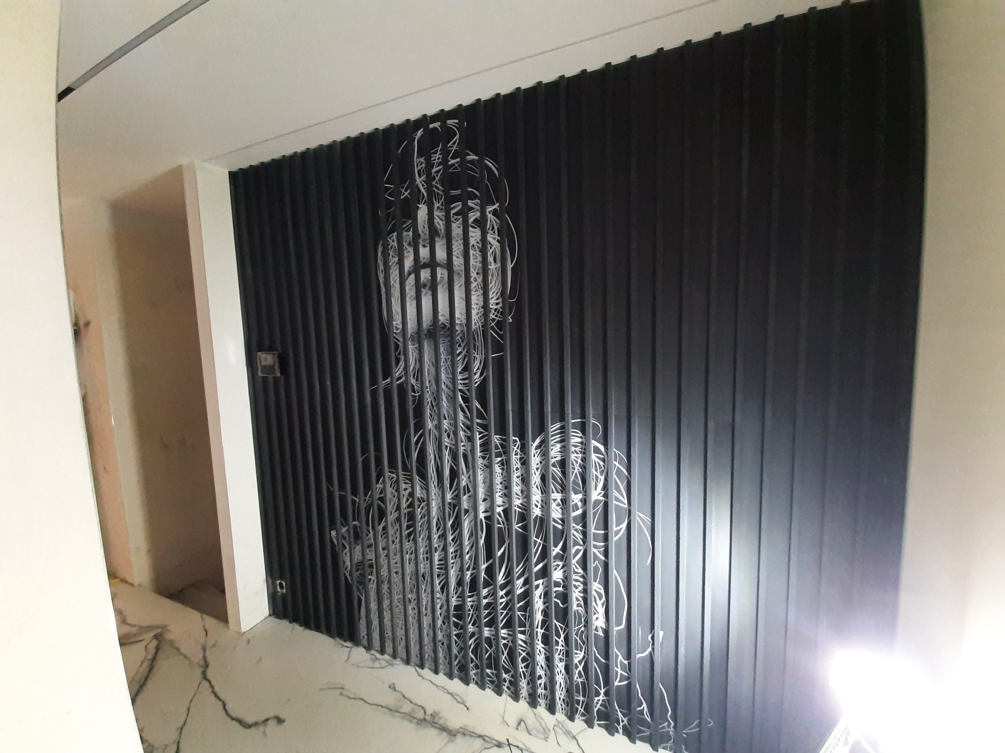 Nowoczesna ściana z czarnych pionowych paneli z abstrakcyjnym białym rysunkiem postaci, marmurowa podłoga w tle, widok z dołu.