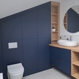 Adrian Paśko ADiMEB - Niebieska szafa na wymiar zabudowana pod skosem w łazience, obok umywalka nablatowa z drewnianym blatem i otwartym regałem, okrągłe lustro.