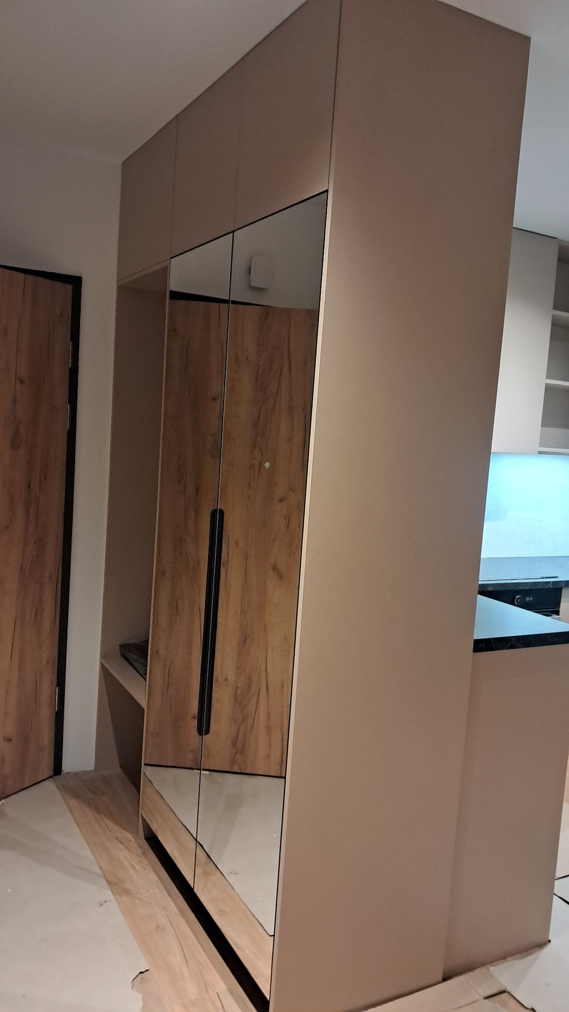 Nowoczesna szafa wnękowa z lustrzanymi drzwiami i drewnianym wykończeniem, wkomponowana w przestrzeń kuchenną.