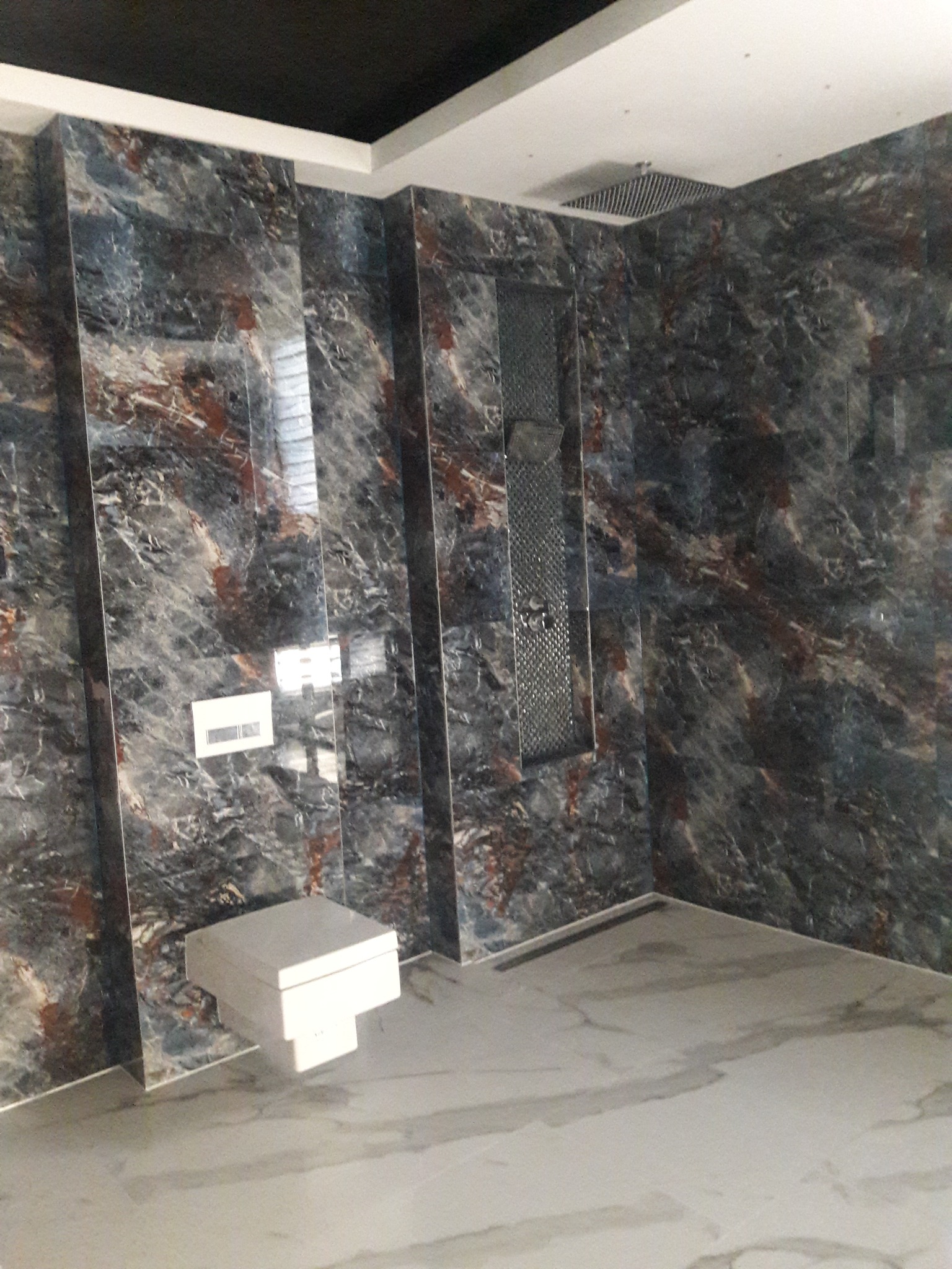 Nowoczesna łazienka z marmurowymi płytkami w odcieniach szarości, brązu i bieli, wyposażona w podtynkowy system spłukiwania i deszczownicę wbudowaną w sufit.