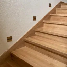 Drewniane schody z oświetleniem punktowym w ścianie o fakturze baranka, widok z dołu.