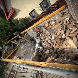 Republika Wolności Sp. z o.o. - Wznoszenie konstrukcji wiaty i tarasu z belek sosnowych i dębowych, widok z góry na plac budowy z porozrzucanymi fragmentami drewna i narzędziami.