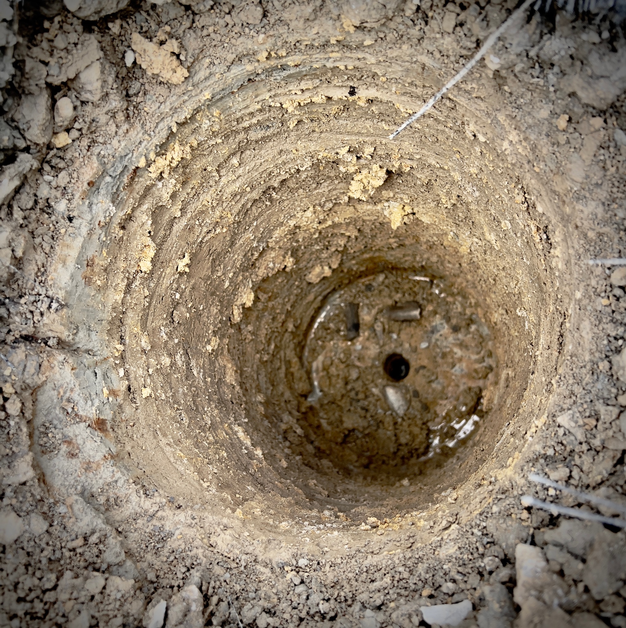 Otwór w ziemi z widoczną podstawą słupa fundamentowego, wypełniony wodą i ziemią, przygotowany pod konstrukcję drewnianą.