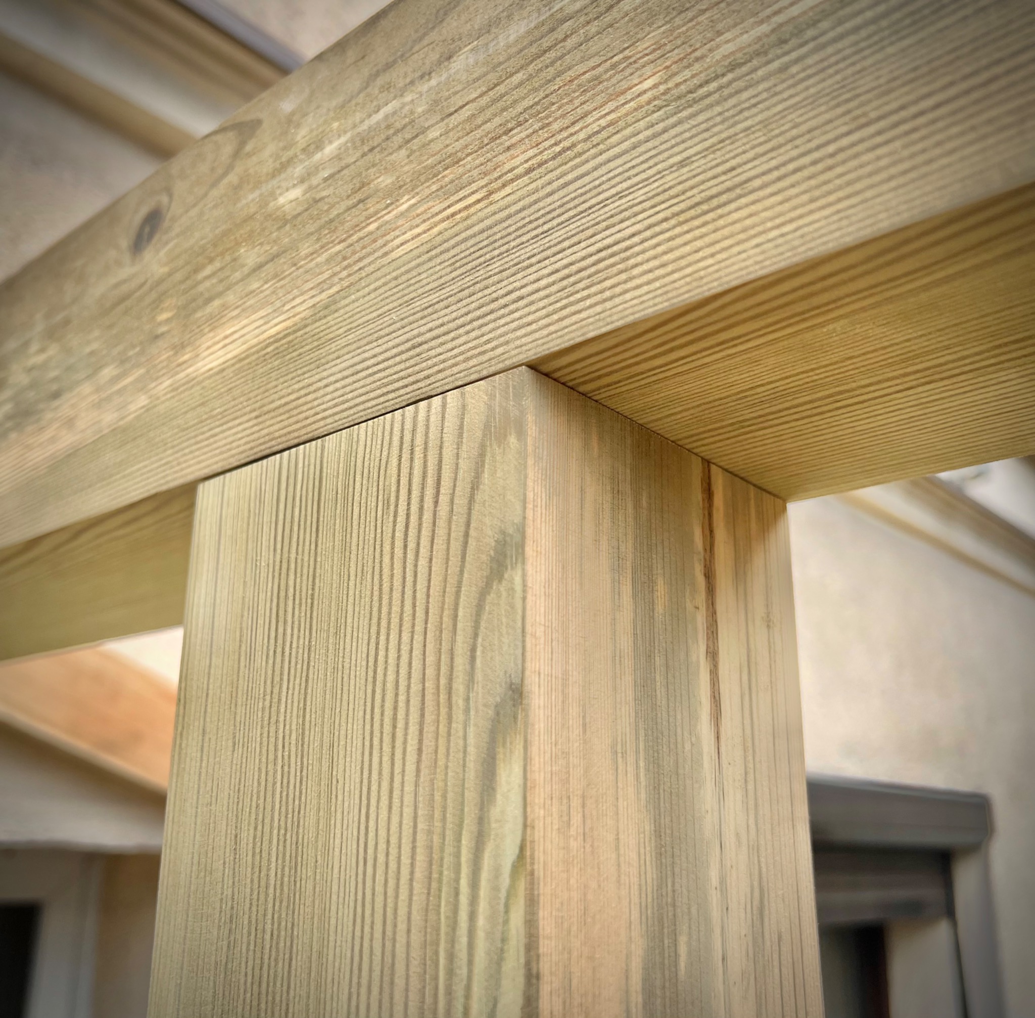 Fragment drewnianej konstrukcji tarasu z widocznym słupem i belką, jasne drewno z wyraźnym usłojeniem, ujęcie z dołu.